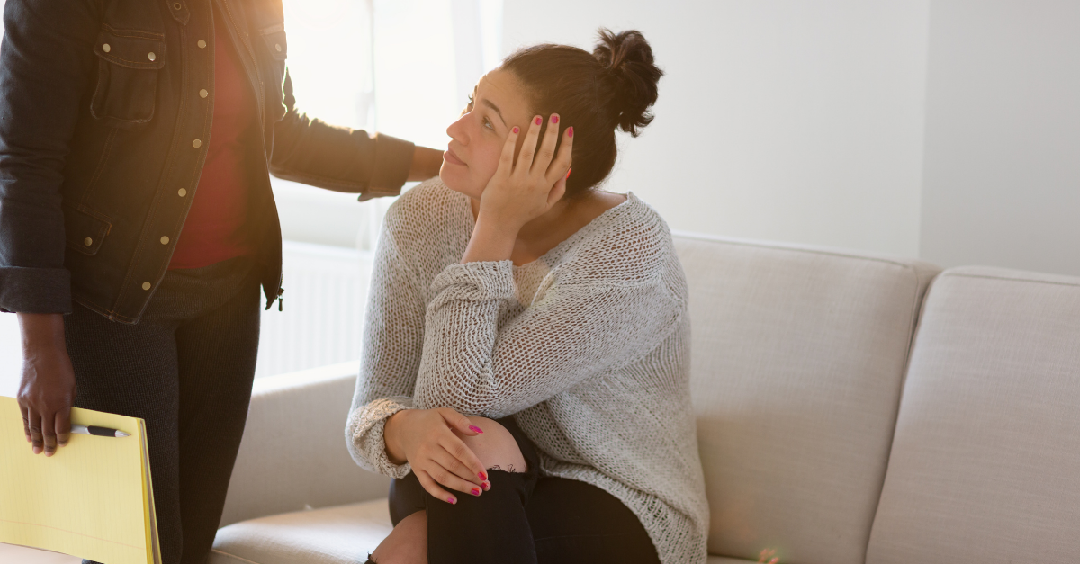 Colleague supporting struggling peer sitting on sofa - hand on shoulder and connecting through eye contact